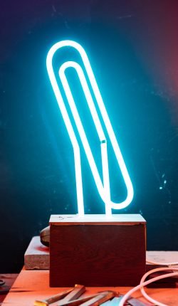 A close-up of a blue neon paper clip light on a wooden base.